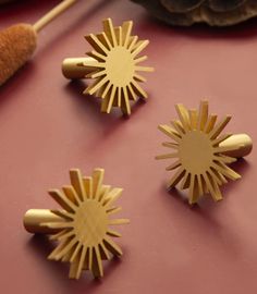 three wooden pins sitting next to each other on a pink surface with pine cones in the background