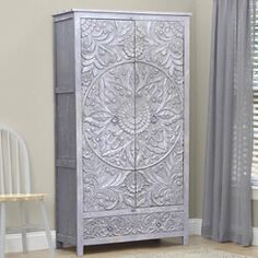 a white cabinet sitting next to a window in a room with curtains and a chair