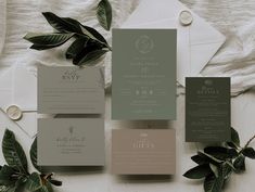 the wedding stationery is laid out on top of the table with greenery and white envelopes