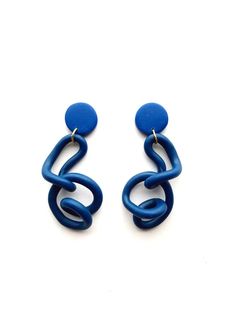 two pairs of blue earrings on a white surface, one is shaped like a spiral