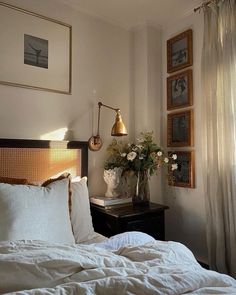 a bed with white sheets and pillows in a bedroom next to pictures on the wall