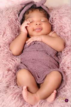 a baby is laying down on a pink blanket with her hands under her chin and eyes closed