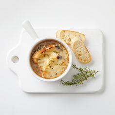 a white plate topped with a bowl of soup and slices of bread on top of it