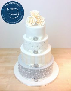 a three tiered wedding cake with white flowers on top and blue ribbon around the bottom