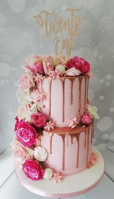 a three tiered cake with pink and white flowers on the side, topped with a gold topper