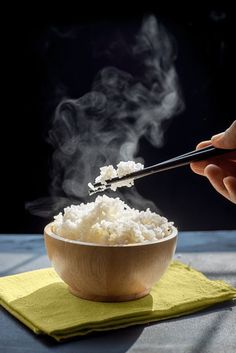 someone is stirring rice in a bowl with chopsticks on the table next to it