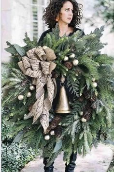 a woman holding a christmas wreath with bells and evergreens on the front, while wearing black boots