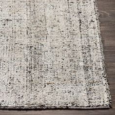 an area rug with white and black colors on top of a wooden floor next to a gray wall