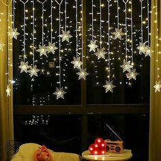 a window with snowflakes hanging from it's side and lights on the outside