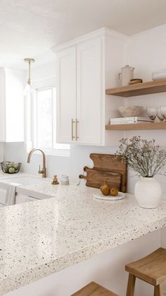 a kitchen with white cabinets and countertops has wooden stools in front of the sink