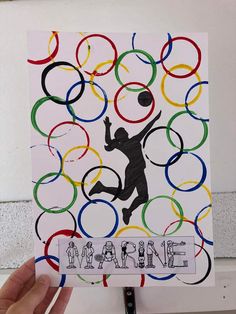 someone is holding up a card with an image of a man playing basketball in the olympic rings