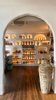 an arched doorway leads into a wine cellar with bottles on the wall and wooden floors