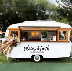 a white and orange food truck parked on top of a lush green field