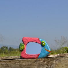 a colorful bird shaped mirror sitting on top of a wooden fence post in front of a blue sky