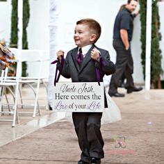 a little boy in a suit and tie holding a sign that says what wish here comes the love of your life