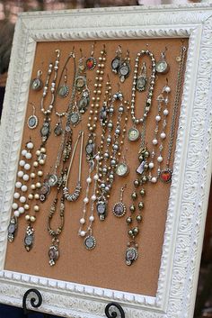 a white frame holding many different types of necklaces and brooches on display