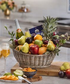 a basket of fruit and two glasses of wine on a kitchen counter with an appetizer