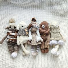 several knitted stuffed animals laying on top of a white blanket, all wearing sweaters and hats