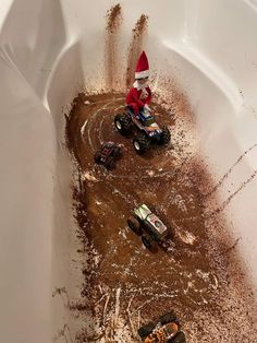 two toy trucks are in the mud and one is wearing a santa hat