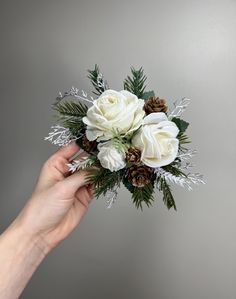 a hand holding a bouquet of white roses and pine cones