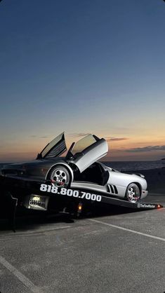 a silver sports car with its doors open on the back of a flatbed trailer