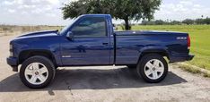 a blue pick up truck parked in a parking lot next to a tree and grass field