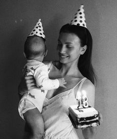 a woman is holding a baby and wearing birthday hats while she holds a cake with candles on it