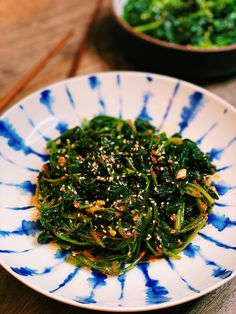 a white and blue plate topped with greens next to a bowl filled with broccoli