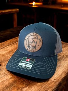 Elevate your style with our Richardson 112 Snapback Trucker Hat, featuring a circular leatherette patch boldly proclaiming, "Blame it on the Whiskey." This hat is designed to make a statement that's as unique as you are, perfect for those who appreciate a touch of irreverent charm. Customizable Options: Patch Placement: Choose between front and center for an in-your-face declaration or off to the left side for a subtle nod to your whiskey-loving tendencies. Color Combos: Select from two striking options to match your style: Charcoal Front, Black Mesh Back: A classic combo that exudes versatility. Navy Front, Charcoal Mesh Back: A bold choice for those who love to stand out. Patch Choices: Personalize your hat further by opting for either a rugged rawhide patch or a suave gray patch. The ch Hat With Patch, Whiskey Lover Gifts, Mens Hat, You Are Perfect, Unique Charms, Black Mesh, Trucker Cap, Color Combos, Hats For Men