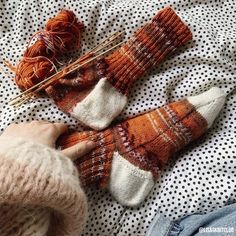 someone is knitting socks on top of a bed next to some yarns and needles