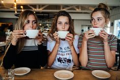 three women sitting at a table drinking from mugs with their hands in front of them