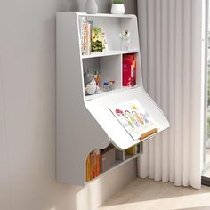 a white book shelf with books and magazines on it in front of a large window