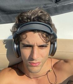 a shirtless man wearing headphones on top of a boat in the sun with his eyes closed