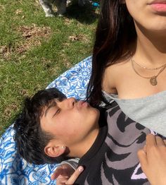 a man and woman laying on a blanket in the grass with a dog behind them