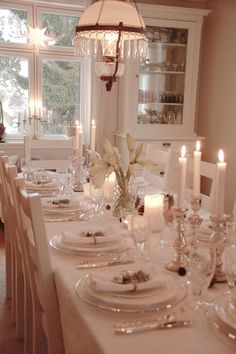 a dining room table is set with white plates and place settings, candles in the center