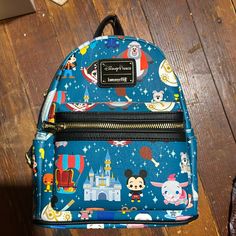 a blue backpack with mickey mouse and other disney characters on it sitting on a wooden floor