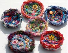 four different types of yarn and buttons in small baskets on top of a white surface