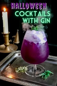 a purple cocktail in a glass on top of a metal tray next to a lit candle