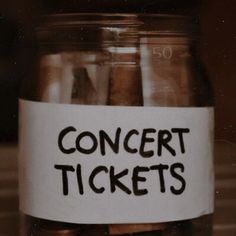 a jar filled with lots of coins sitting on top of a wooden table next to a sign that says concert tickets