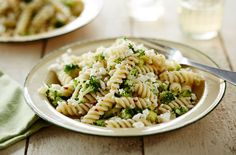 pasta with broccoli and feta cheese on a plate next to a glass of water