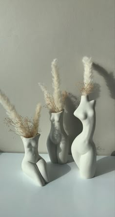 three white vases with dried plants in them