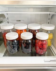 several jars filled with different types of fruit in an open refrigerator freezer door,