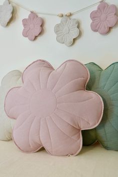 three pillows with flowers on them are sitting on the bed in front of a string of bunting