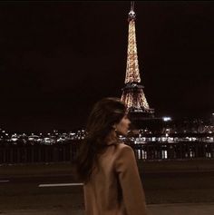 a woman standing in front of the eiffel tower at night with her back turned to the camera