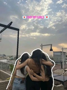 two women hugging each other on top of a roof with the sky in the background