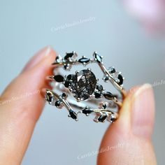 a woman is holding a fancy ring with black stones on the sides and silver accents