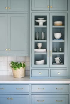 a kitchen with blue cabinets and white dishes on the counter top, along with a potted plant