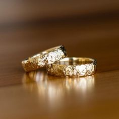 two gold wedding rings sitting on top of a wooden table