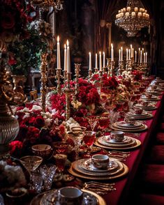 a long table is set with red flowers and silverware for a formal dinner party