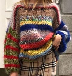 a woman is walking down the street wearing a multicolored sweater and plaid pants